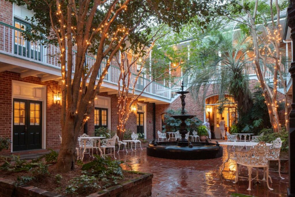 a classic louisiana style out door courtyard complete with trees with fairy lights, a fountain and white wrought iron tables and chairs
