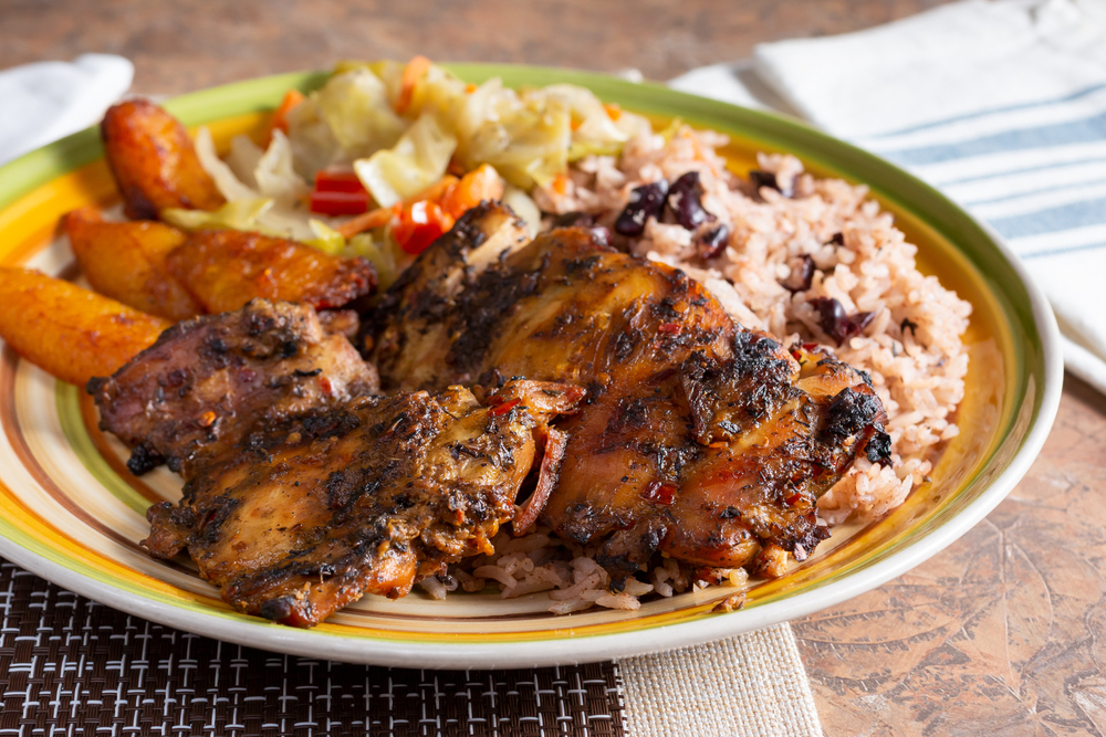 A plate of Jamaican food like fried plantains, black beans and rice, jerk chicken, and a salad its similar to what you'll find at some Black owned restaurants in Washington DC