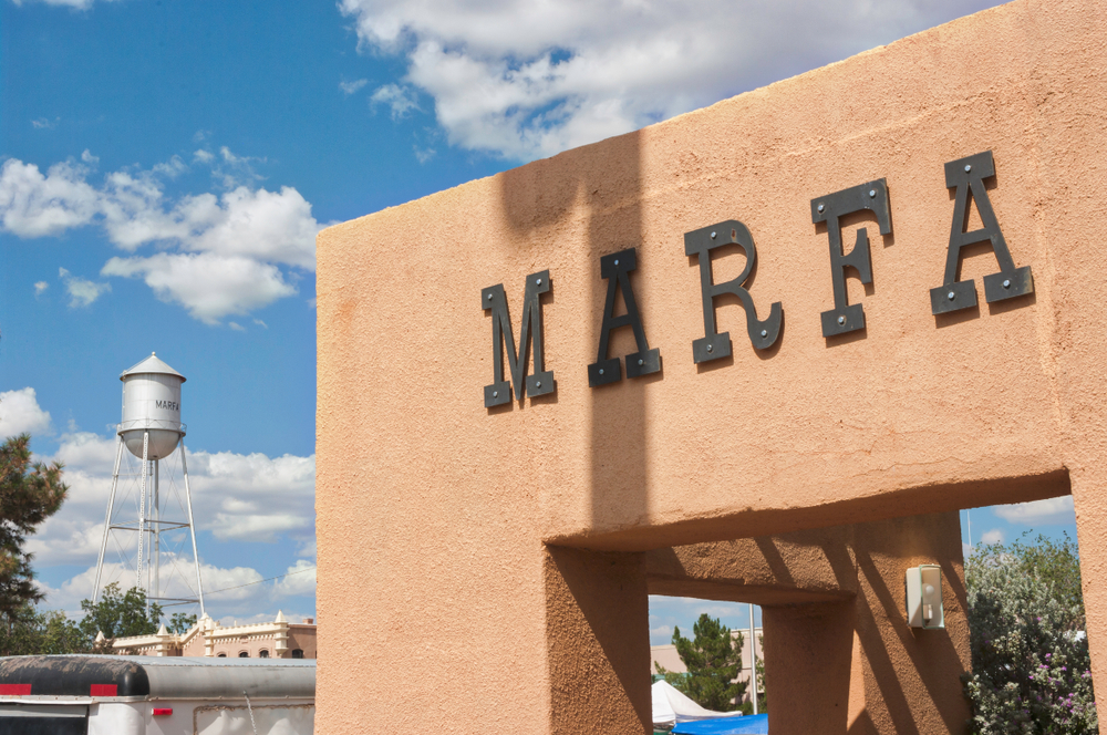 The exterior of a terracotta stucco building with letters that say 'Marfa' on it. In the background you can kind of see a city. One of the best hidden gems in Texas. 