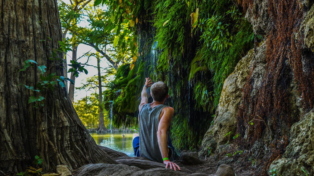 A person sitting at the edge of a natural spring in Texas, pointing at a small waterfall. 