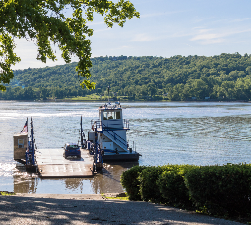 a car on a car ferry in the water, rolling hills in background