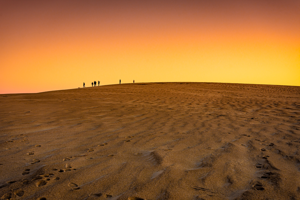 people standing on sand dunes at sunset in jockeys ridge state park, one of the best things to do in nags head north carolina