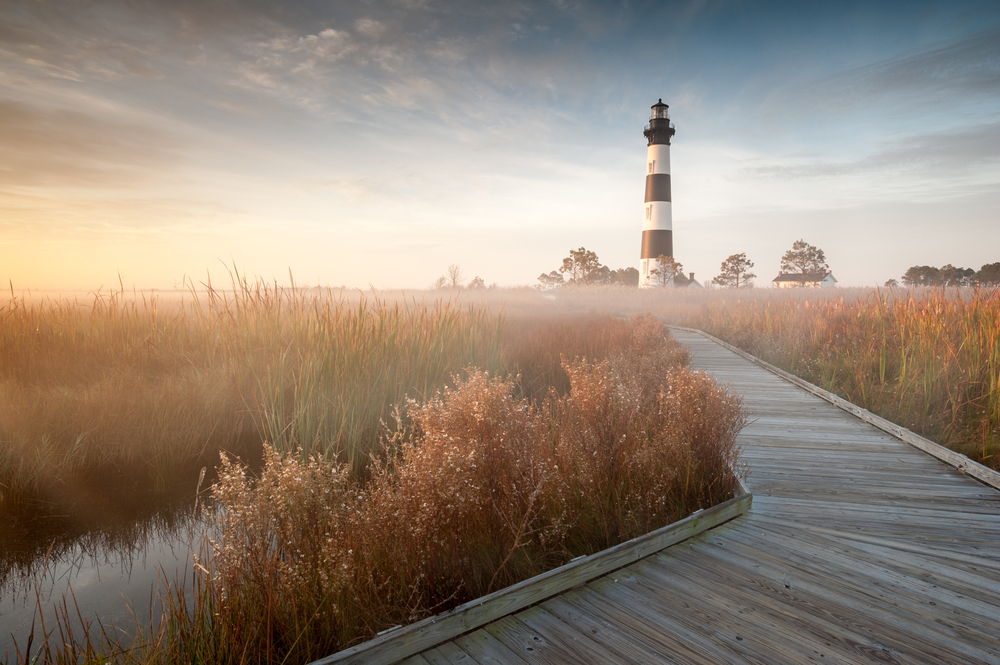 wooden boardwalk through marshland with striped lighthouse in background, things to do in nags head 