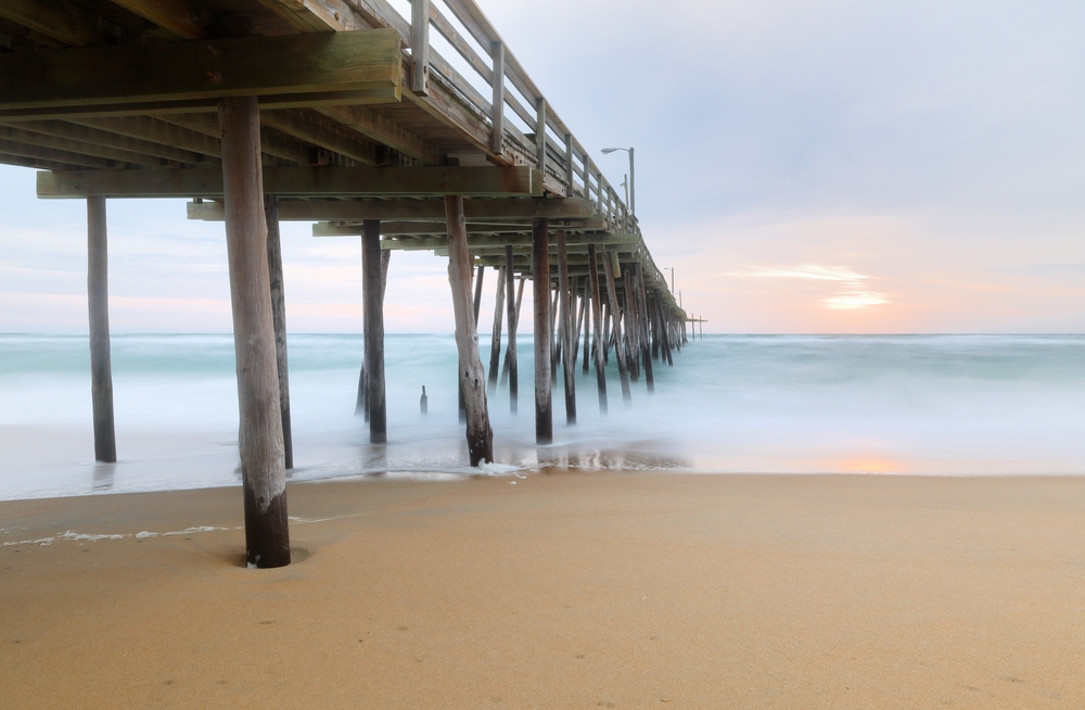 under pier on beach with waves rolling in at sunrise, best things to do in nags head