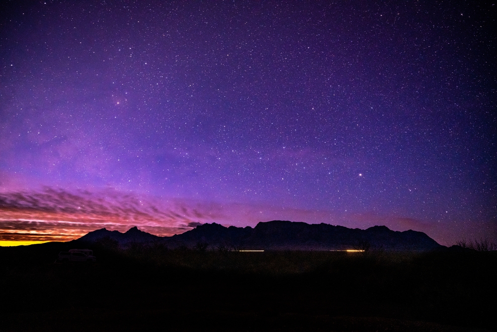 Sunlight and Car Lights Below Night Sky and Chisos Mountain Range in Big Bend National Park. One of the best getaways in Texas