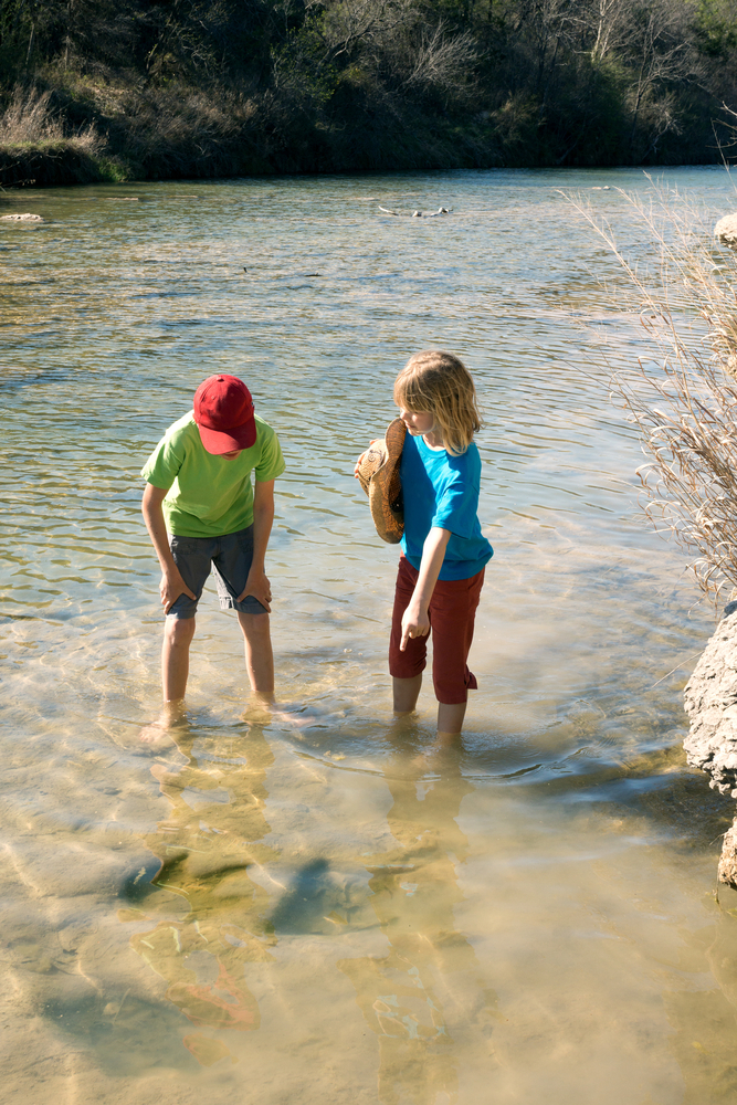 Children curiously looking at the fossilized dinosaur tracks in the river. White Blaff Creek, Dinosaur Valley State Park, Glen Rose,