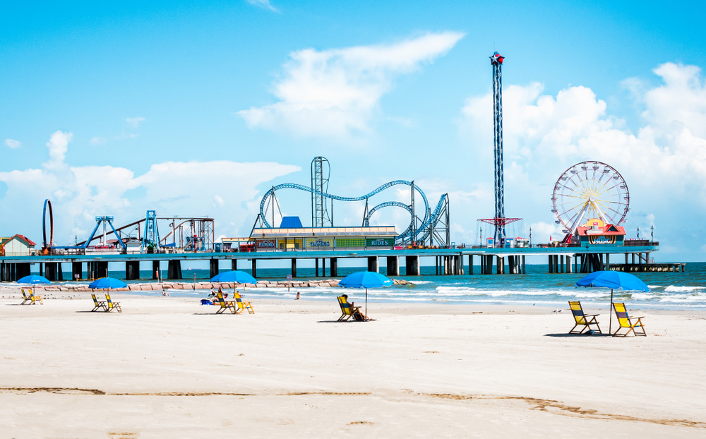 View of beach umbrellas and Pleasure Pier amusement park on Galveston Island. One of the best weekend getaways in Texas