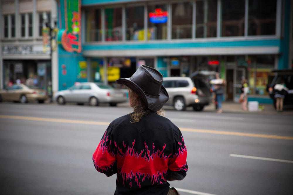 A man stands in the streets of Midtown, knowing where to stay in Nashville. His cowboy hat and black shirt that has pink flames on it stands out against the crowded strip of restaurants in Midtown. 