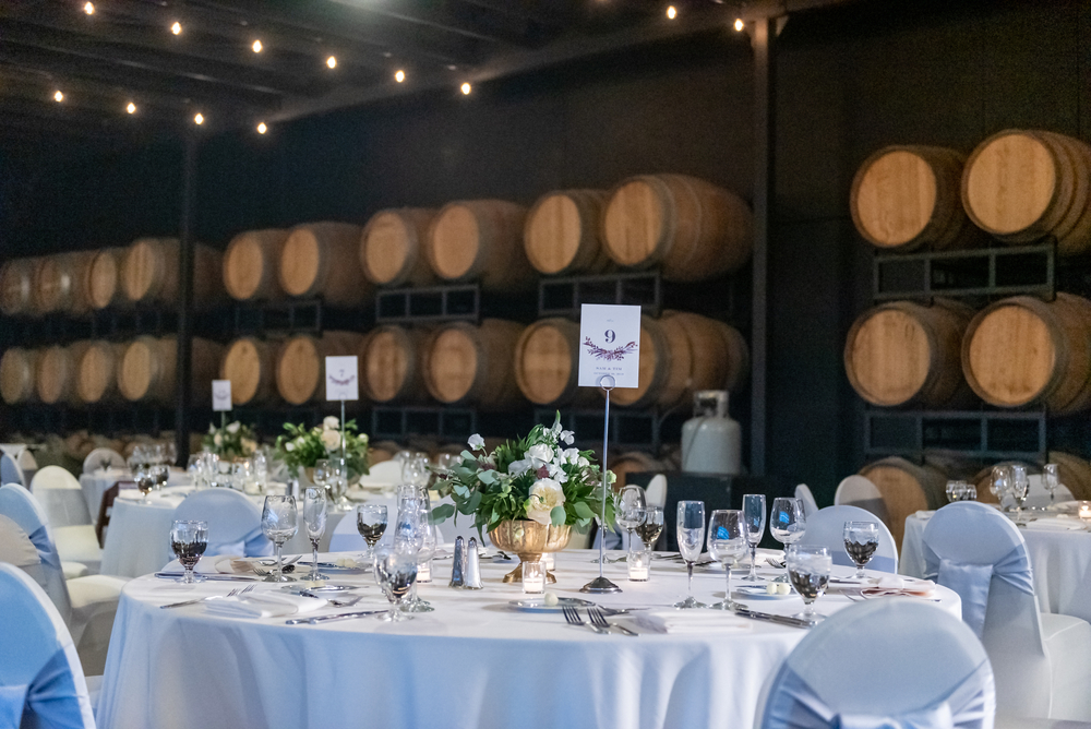 fancy tables set for a meal with wine barrels stacked in the backgronud 