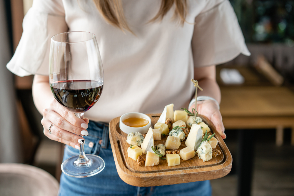 woman holding wine glass and a tray of cheese and nutes