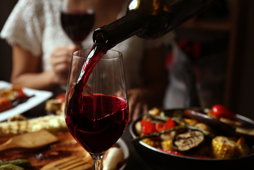 wine being poured into a glass on a table with food in the background