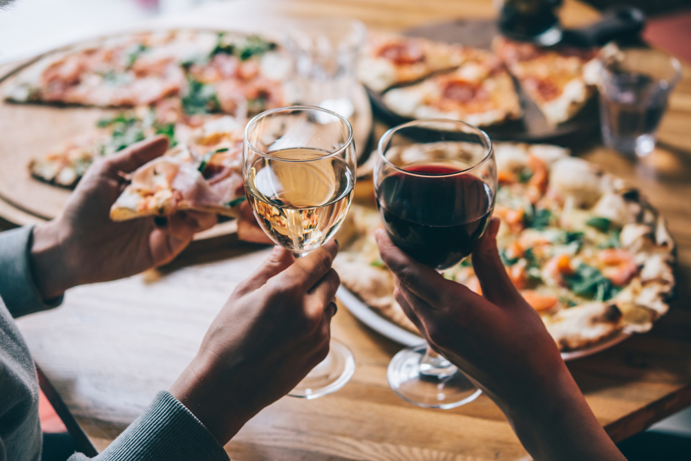 two hands holding two wine glasses with pizza on the table in the background . painted horse winery and vineyard one of the greatest wineries in georgia 