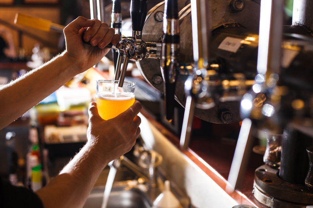 Someone fills a glass of beer from a tap behind a bar.