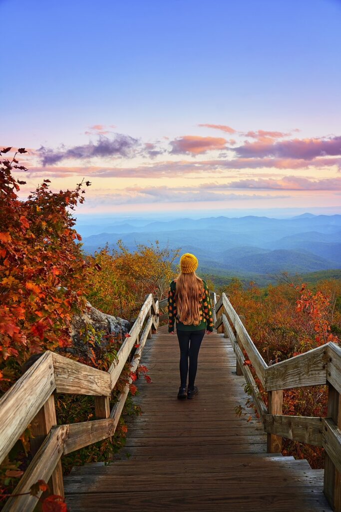 Woman in a fall sweater stands on the stairs of the Rough Ridge Overlook at sunset near Boone.