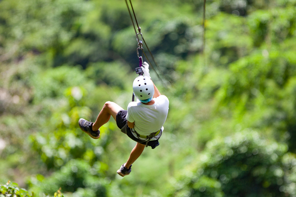 Man going down a zip line in a forest.