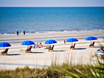 people sitting on a Hilton Head beach with blue umbrellas and white sand
