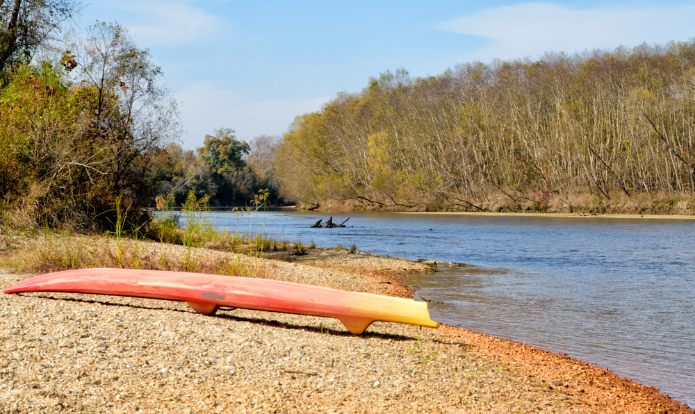 photo of an orange and red paddle boat on the rocky beach at Bogue chitto state park along the waters edge 