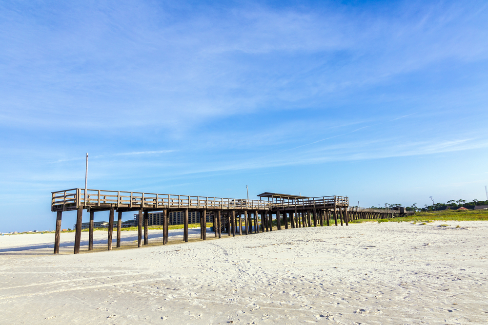 photo of a wooden pier surrounded by sand on dauphin island, one of the beaches near New Orleans 