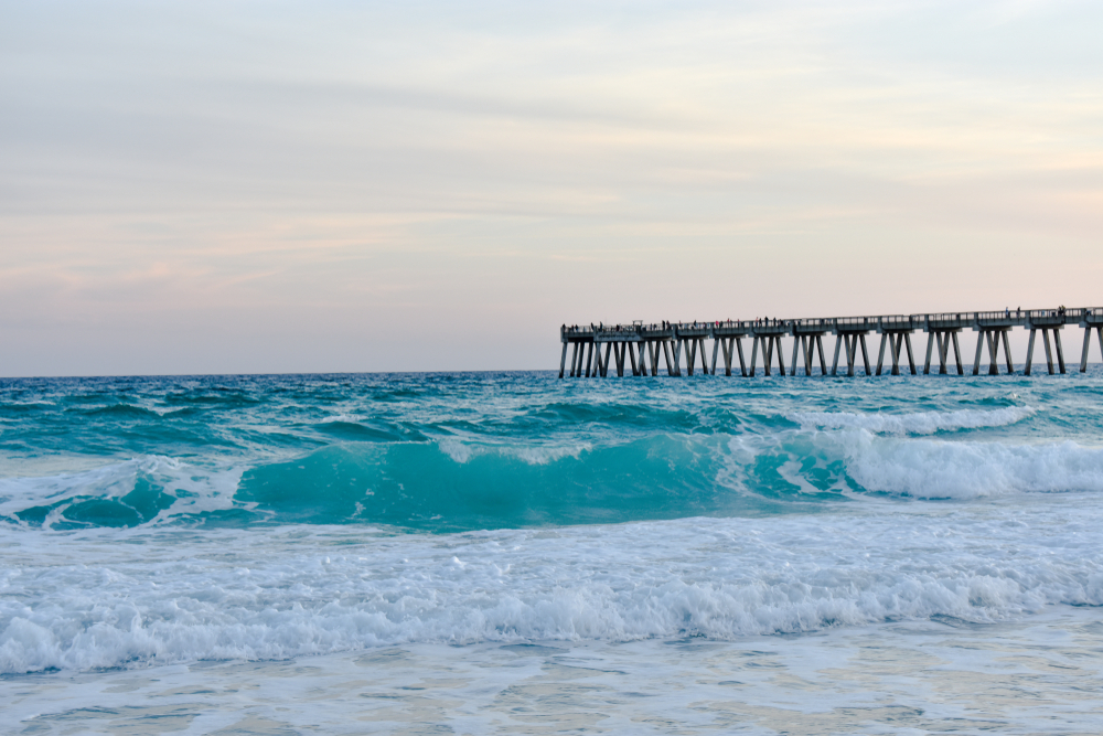 photo of waves crashing on the shore at Navarre beach, with a pier in the background 