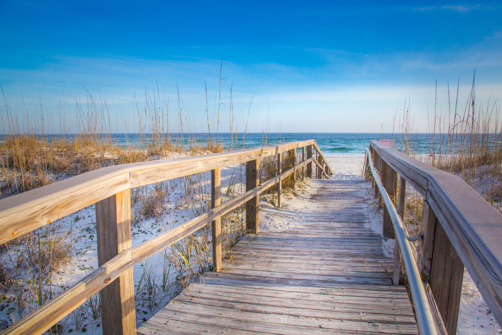 photo of a wooden boardwalk going toward the shoreline at pensacola beach with a view of the water