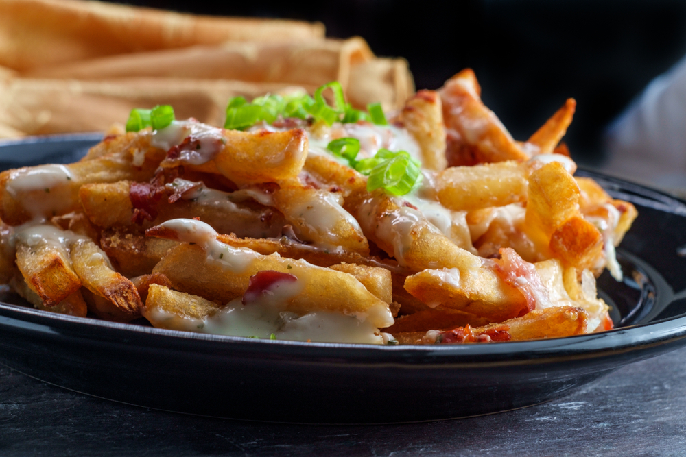 a plate of fries with bacon, onion, and cheese on them 