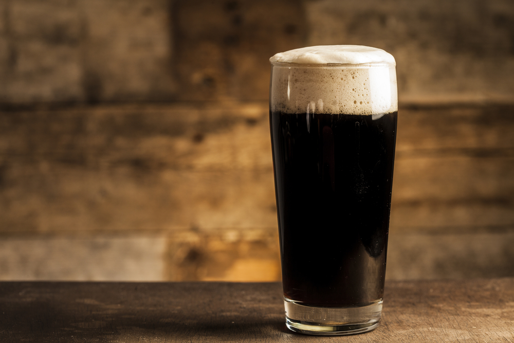 a glass of super dark beer with foam on top sitting on a table