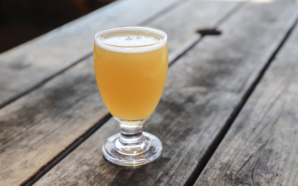a glass of light beer with bubble on top sitting on a wooden picnic table
