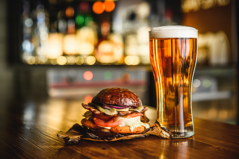 a tall glass of beer next to a burger on the table, natahala brewing, one of the best places for beer in north carolina