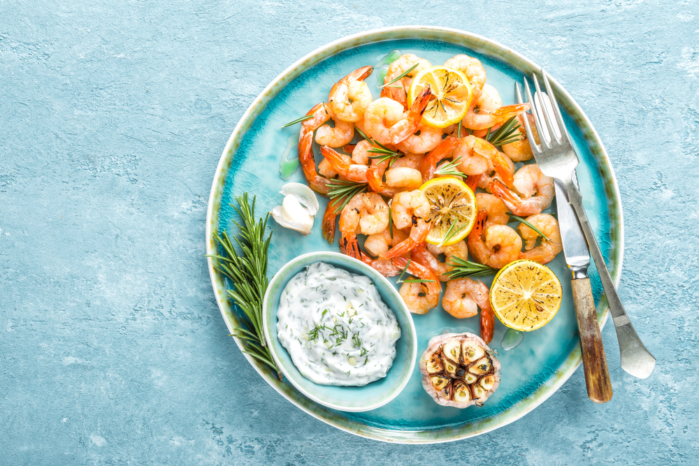 a beautiful clean blue plate of shrimp, topped with garnish of lemons and rosemary with dill tzatziki and roasted garlic!