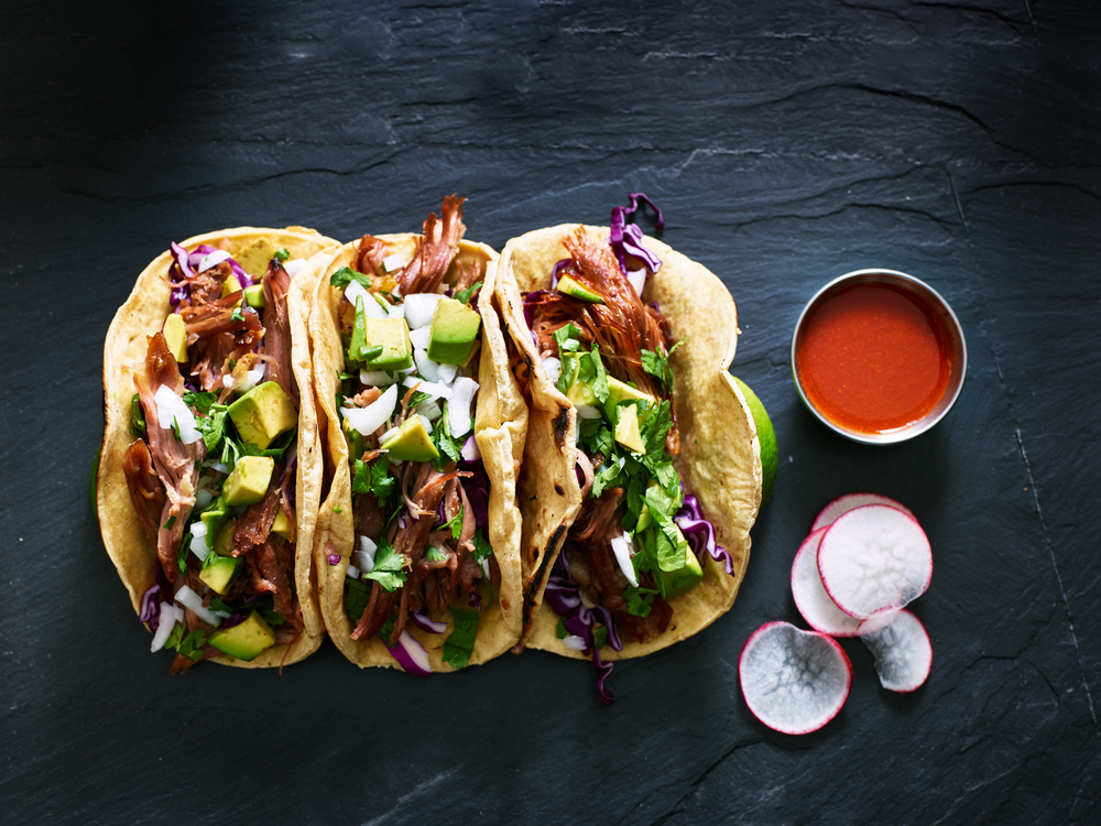 three tacos made with onions, pulled pork, avocados and cilantro with a side of sliced radish and sauce, delicious mexican food to be indulged at some of the best restaurants in Wilmington!
