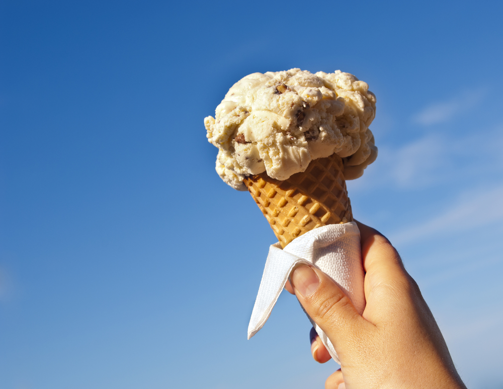 a hand holding an ice cream cone with one scoop of ice cream on top, a napkin is wrapped around the cone