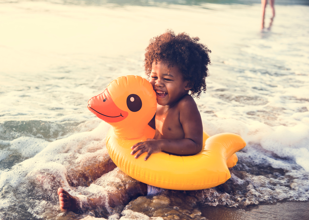 A little boy sitting in a yellow duck on the shore 