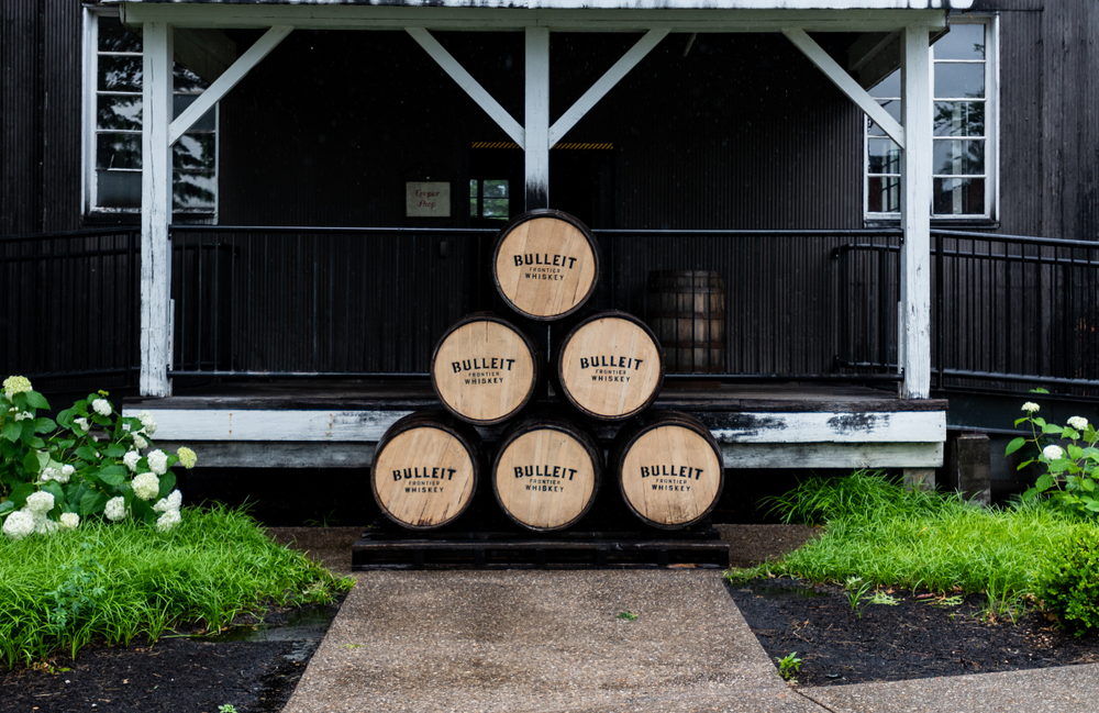 barrels stacked up in front of building with sidewalk in foreground