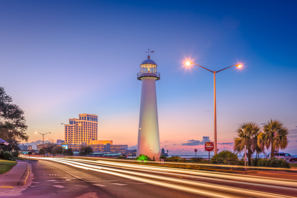The Biloxi Lighthouse at sunset, with streetlights and headlights glowing, with the Beau Rivage Resort in the background.