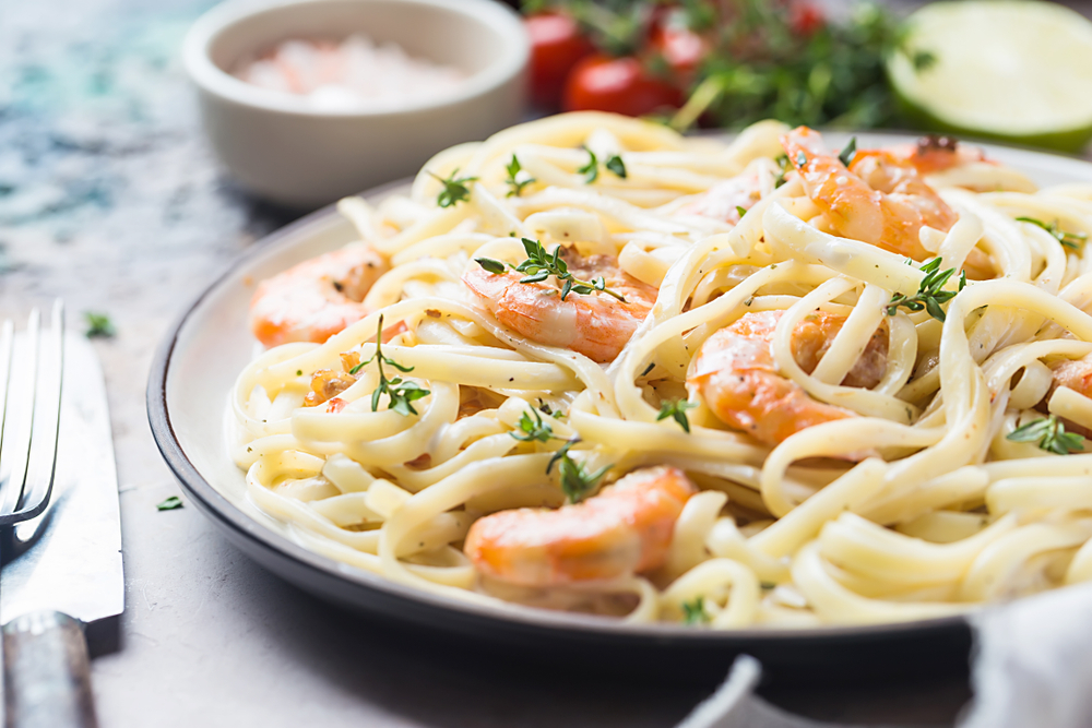 shrimp alfredo on a table with a fork and a knife next to the plate 