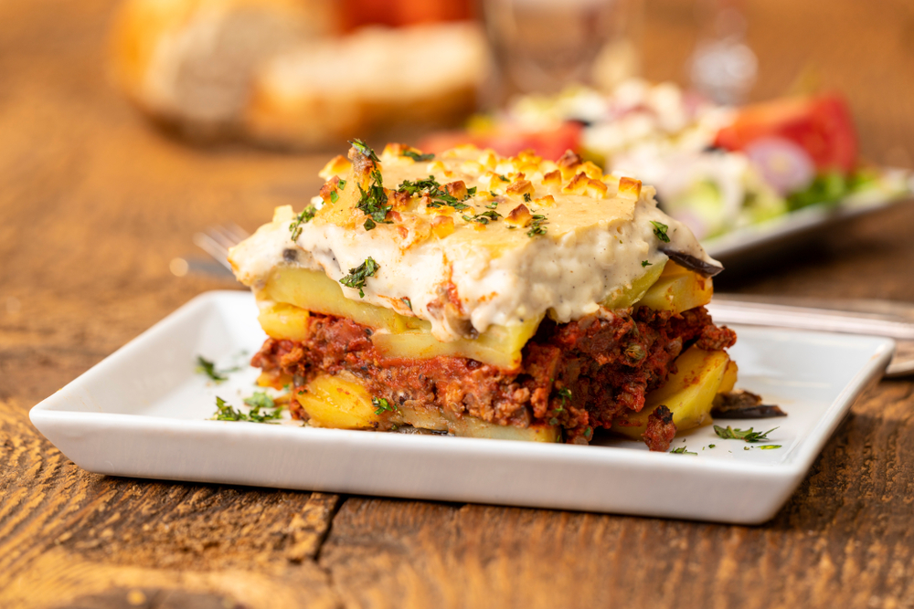 moussaka on a square plate on the table with a fork and knife next to the plate