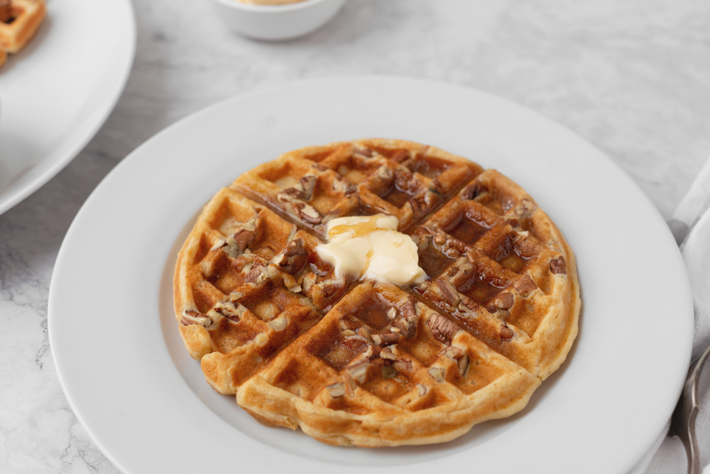 a waffle with butter, syrup, and pecans on top