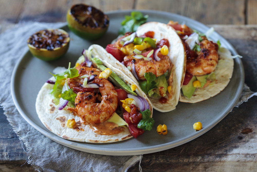 three shrimp tacos on a plate with charred citrus fruit