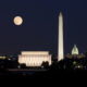 The Lincoln Memorial, Washington Monument, and the Capitol Building at night with a full moon hanging over them, one of the best things to do in Washington DC at night