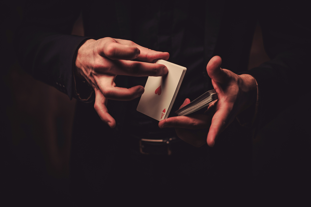 A closeup of hands doing a card trick surrounded by darkness