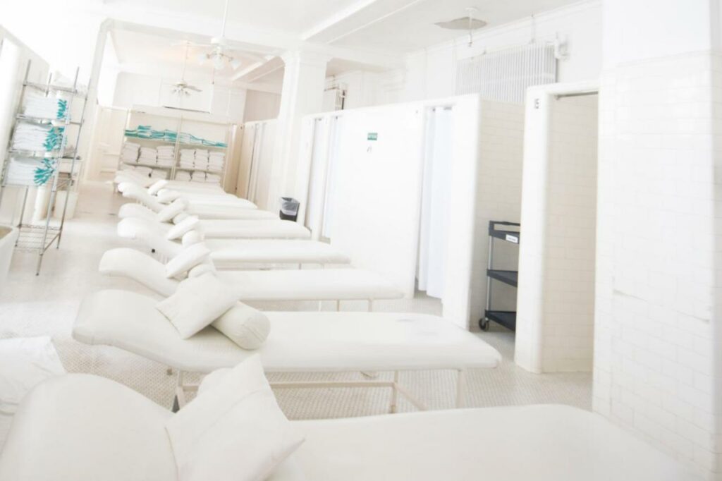 inside of a hotel spa, beds aligned in a row and shelves with towels on them 