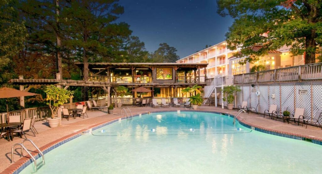 large pool in the fore ground with tables and chairs around the pool, hotel in the background