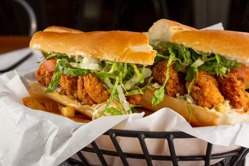 close up photo of a shrimp po boy in a basket with lettuce, sauce, and tomatoes, 