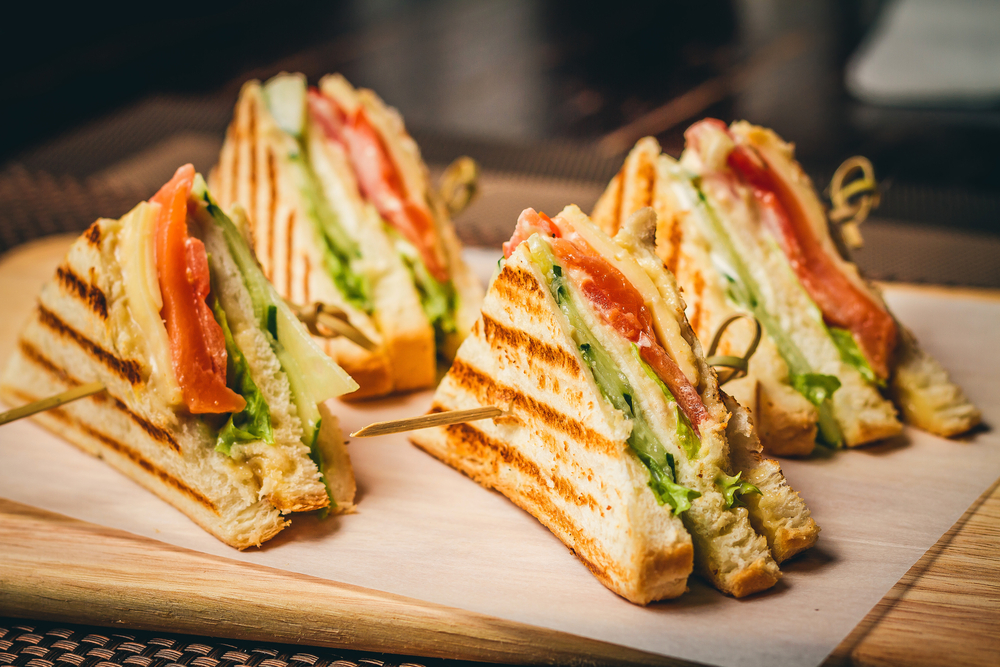 four triangles of a sandwich sit on a paper on a wooden plate, toothpicks through the trainagles