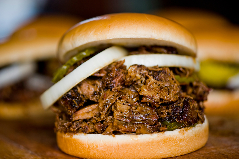 a brisket sandwich with onions and pickles on it, more sandwiches in the background. 