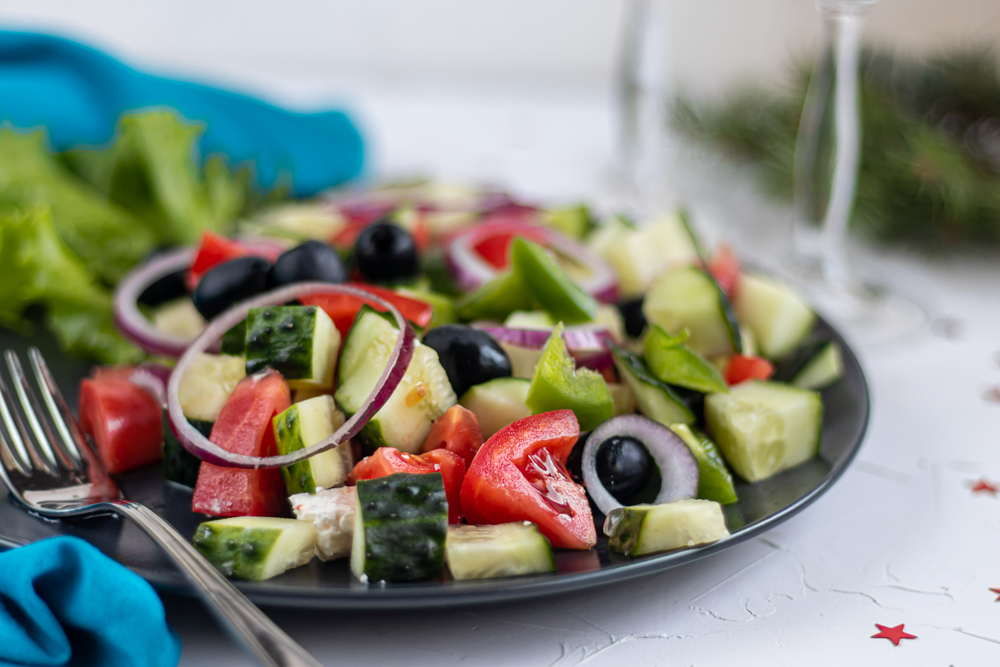 a fresh salad of cucumbers, tomatoes, olives, feta, and red onions on a table