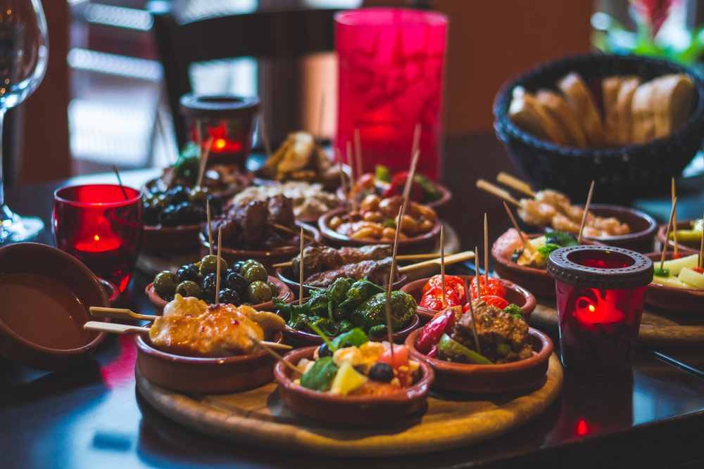 spanish tapas in small bowls on a table withe candles and a basket of bread