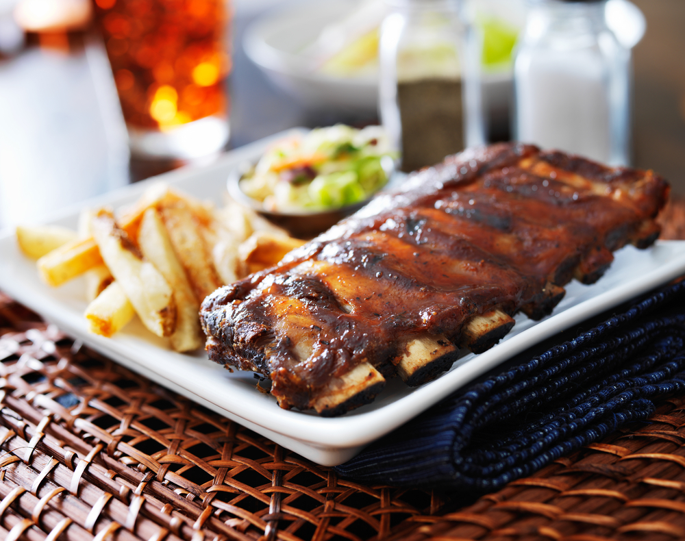 a plate with baby back ribs, french fries, and cole slaw on it on an outdoor table in a patio area 