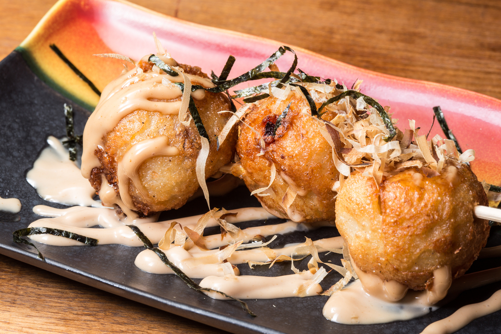 three tako yaki on a small plate on a wooden table from thaicoon and sushi bar 