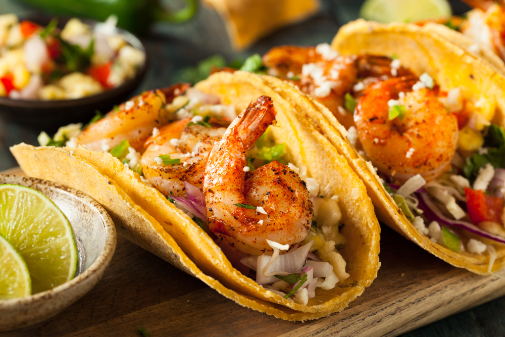 one of the best things to do in brunswick, marshside grille, a wooden plate with three shrimp tacos next to a bowl of lime wedges